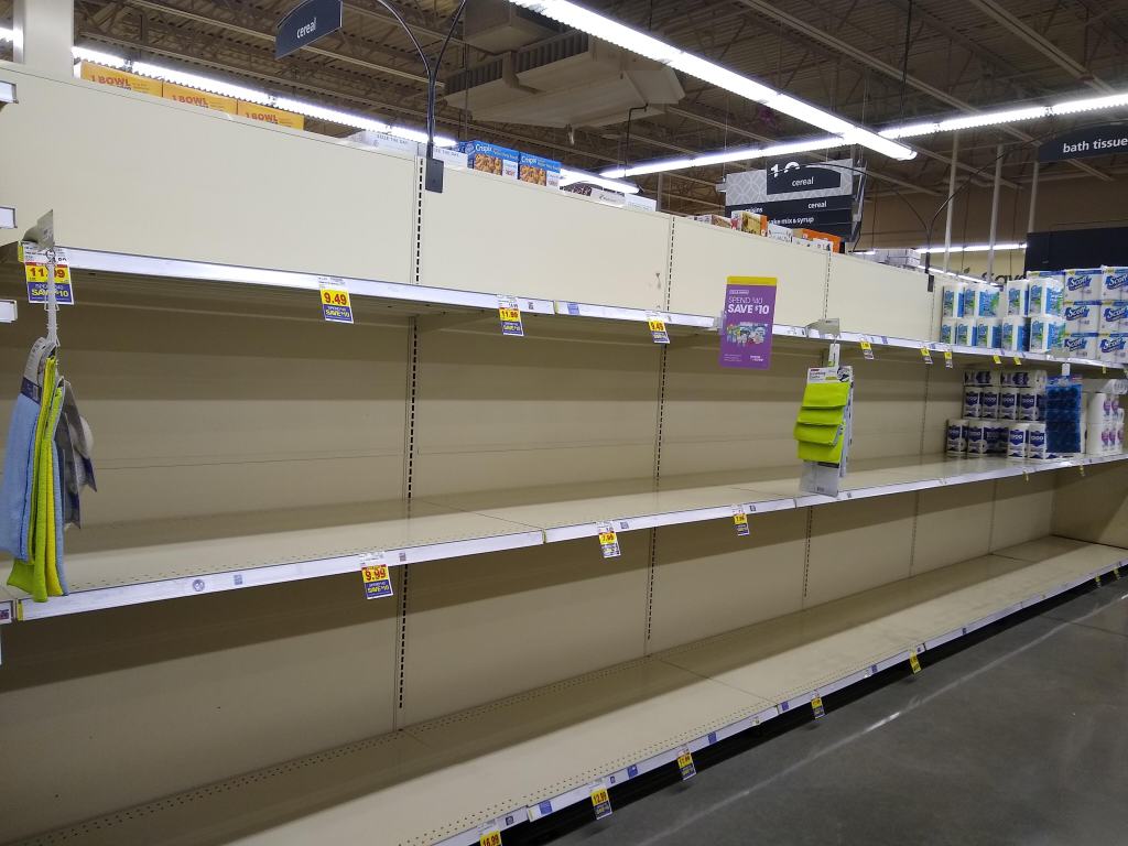 Shelves in a grocery store, almost completely denuded of toilet paper.